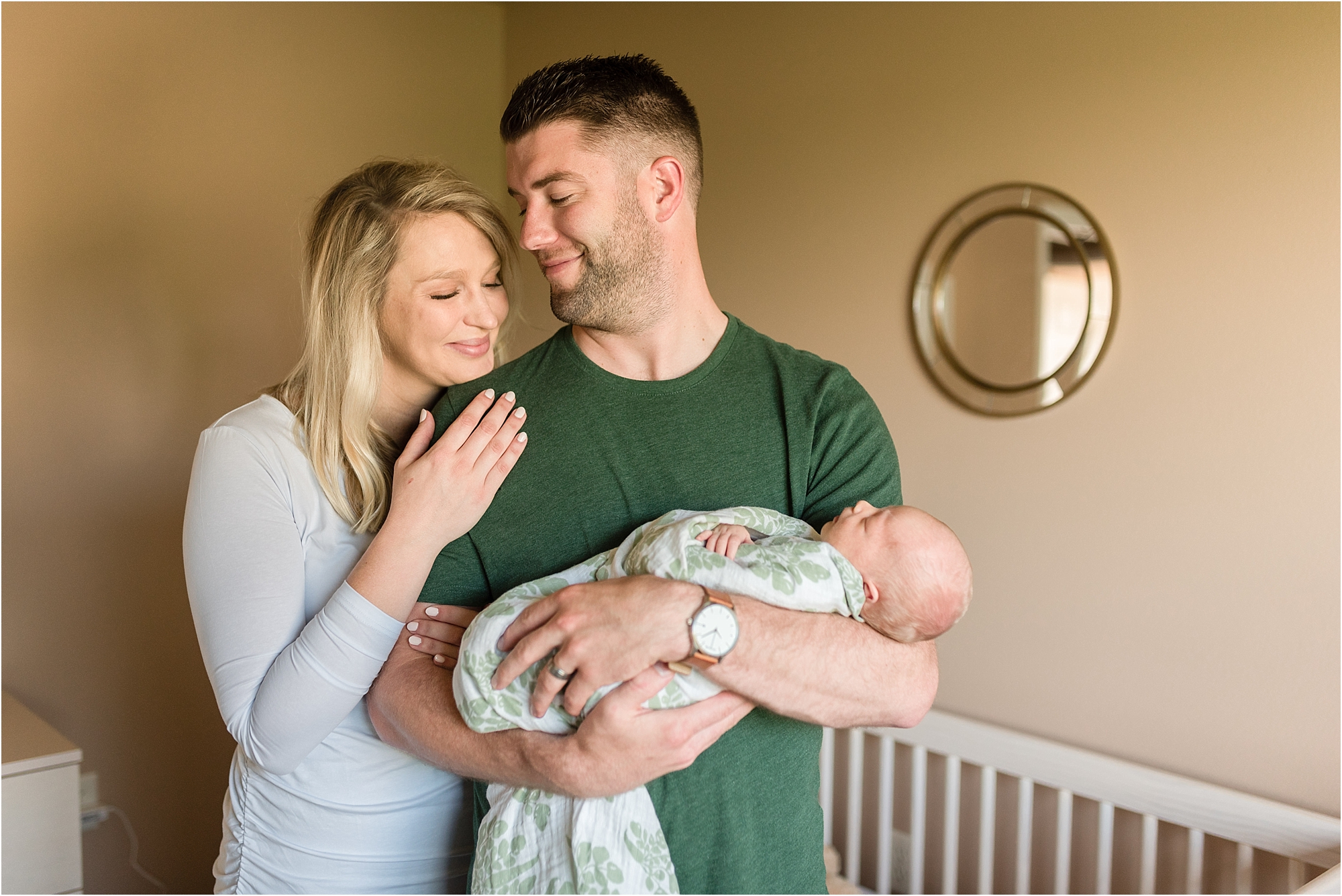 mom and dad looking at each other holding new baby in nursery