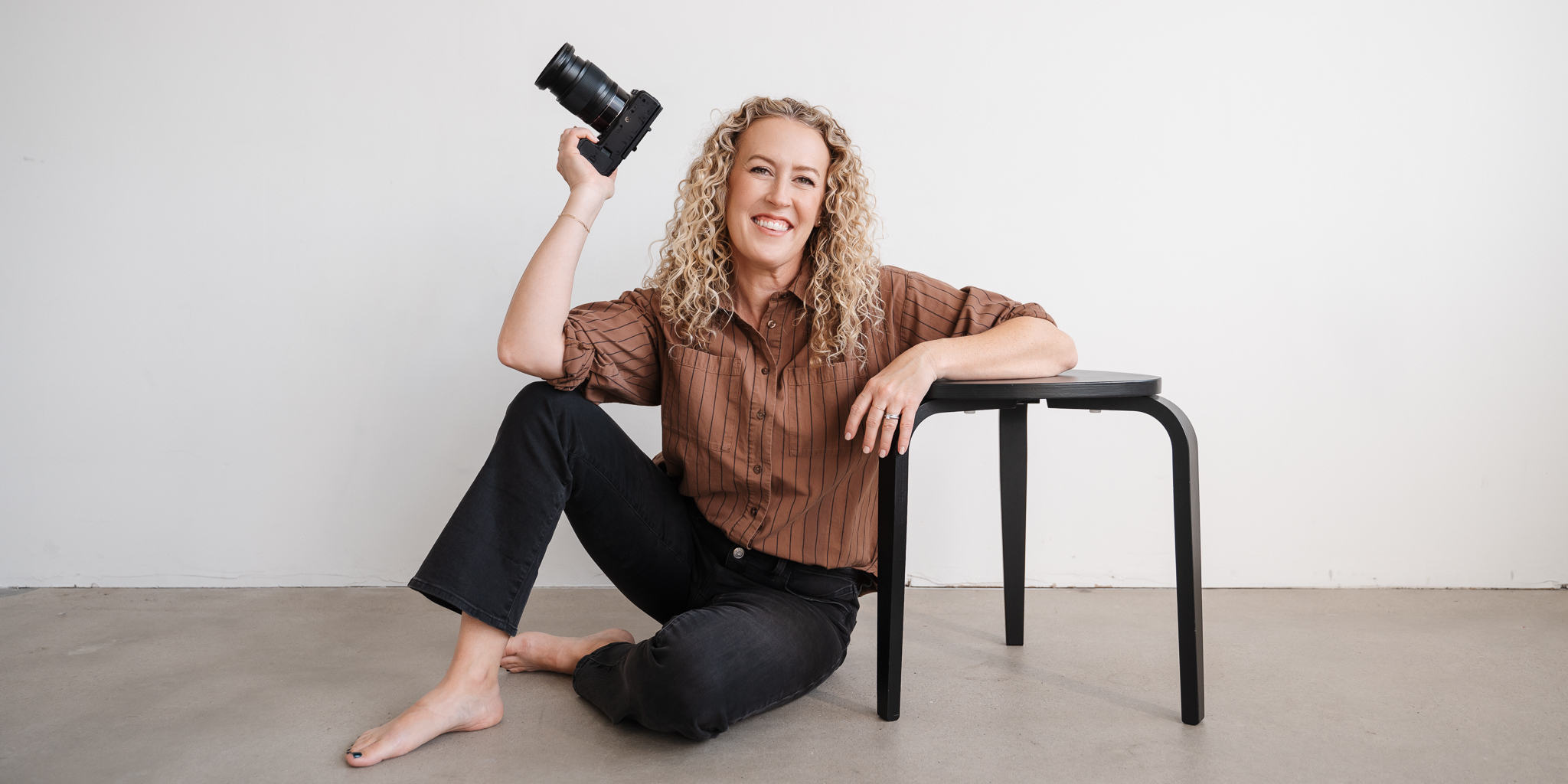 Jill Neil leaning on black stool with camera